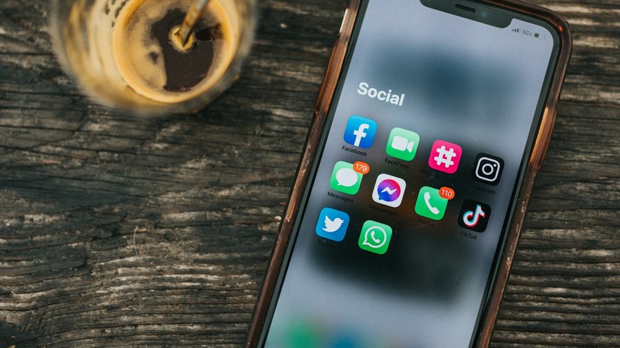 木の机に置かれた、SNSのアプリが並ぶスマートフォン