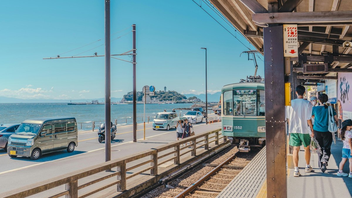 江ノ電の駅のホームから見える海と江の島。人が歩いている